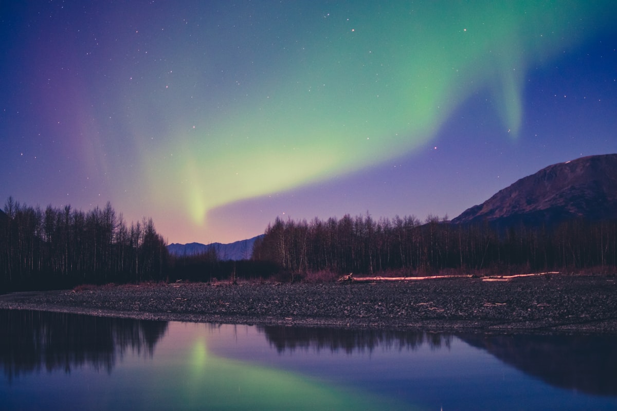 The green and violet northern lights over an Alaskan mountain and river